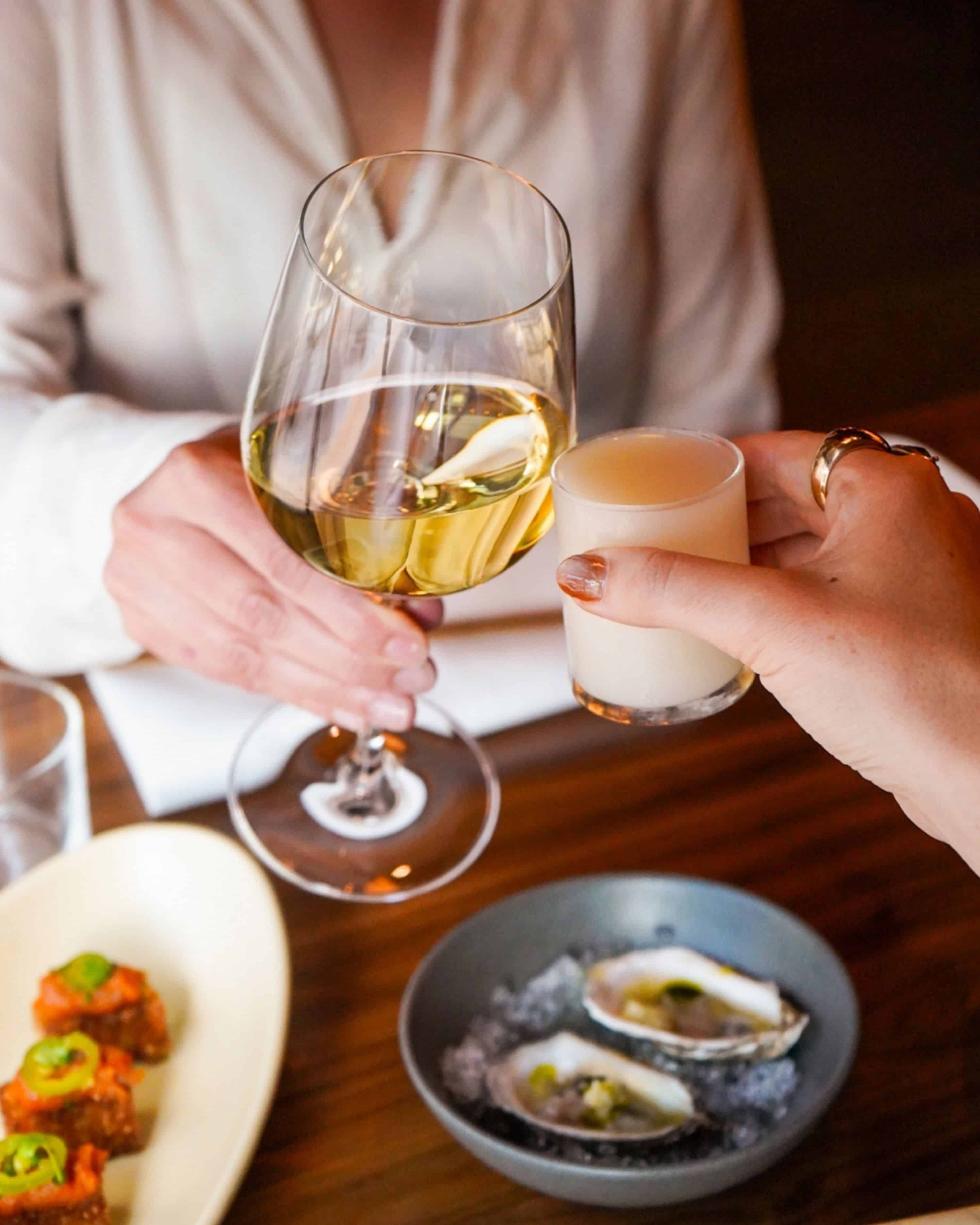 wine glass and sake glass cheersing over a plate of oysters