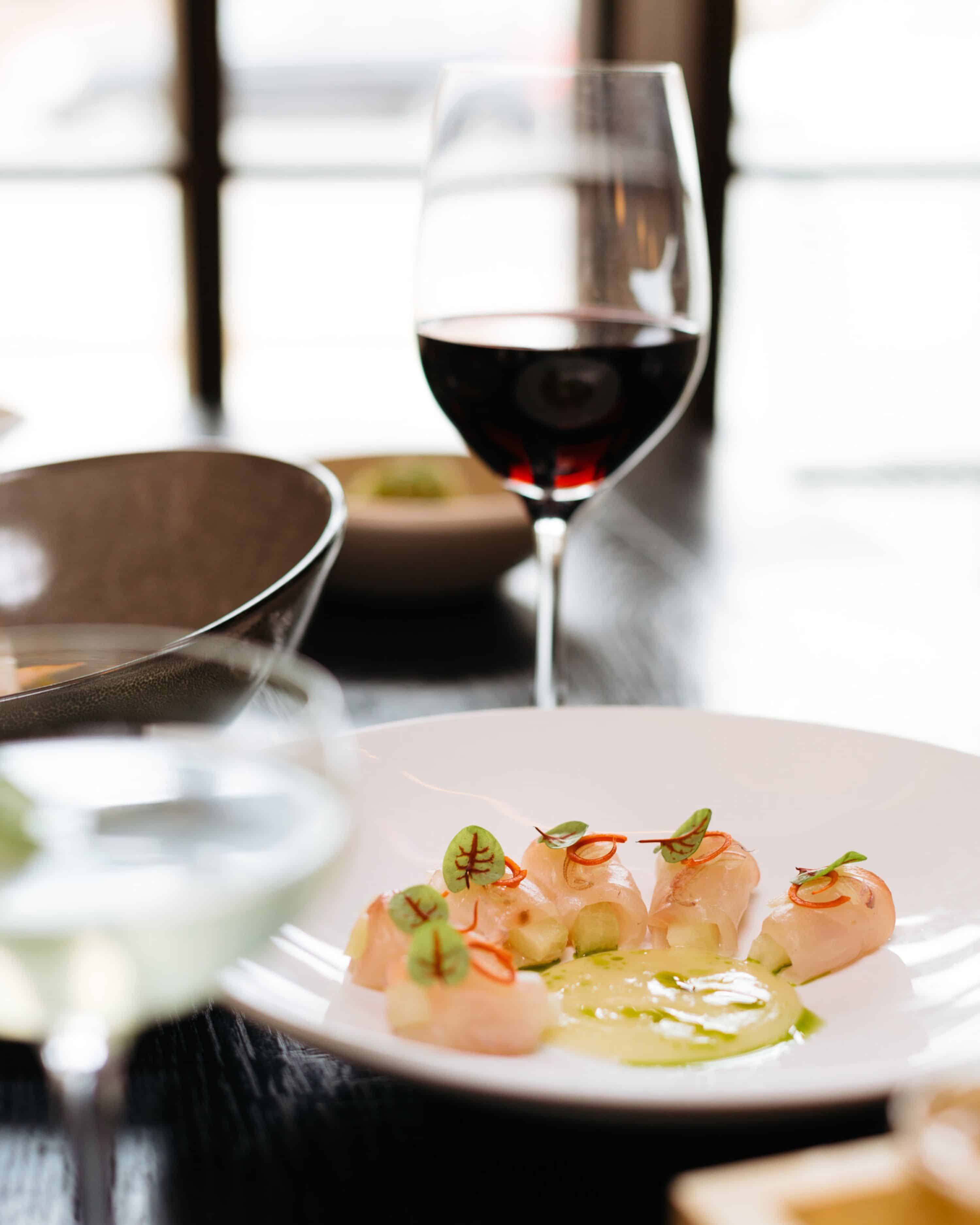 glass of red wine behind a plated crudo