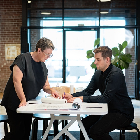 Two people sitting at a table in an office discussing an interior design project.
